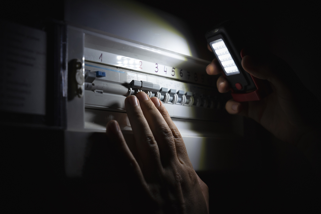 Person using a light to see their switchboard panel during power outage. They are in need of a backup generator install.